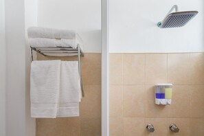 A bathroom with a towel rack holding two towels, a showerhead, and a soap dispenser on the wall.