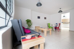 A modern living room with a grey sofa, a wooden coffee table, and a dining area with a white table and colorful chairs.