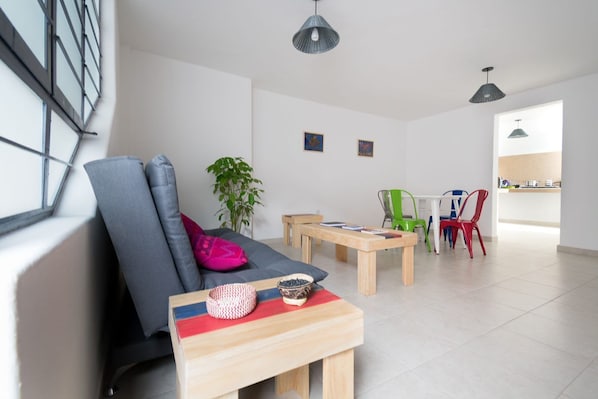 A modern living room with a grey sofa, a wooden coffee table, and a dining area with a white table and colorful chairs.