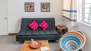 A modern living room with a dark sofa, a wooden coffee table, and a colorful chair. There are two framed pictures on the wall and a ceiling light fixture. - Oaxaca at your doorstep (Oaxaca)