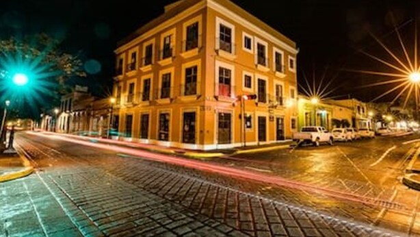 A multi-story building with a yellow facade, a cobblestone street, and streetlights. - Oaxaca at your doorstep (Oaxaca)
