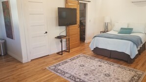 A bedroom with a bed, a TV on a stand, a wooden door, and a patterned rug. - Cozy Private Casita (Tucson)