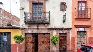 Um edifício com duas portas de madeira, uma varanda com grade de ferro forjado e uma pequena árvore em vaso.