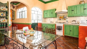 Cozinha com armários verdes, mesa de vidro e painel de azulejos.