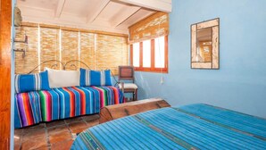 Une pièce avec un mur bleu, un banc en bois, un canapé coloré à rayures et un petit bureau avec une chaise.
