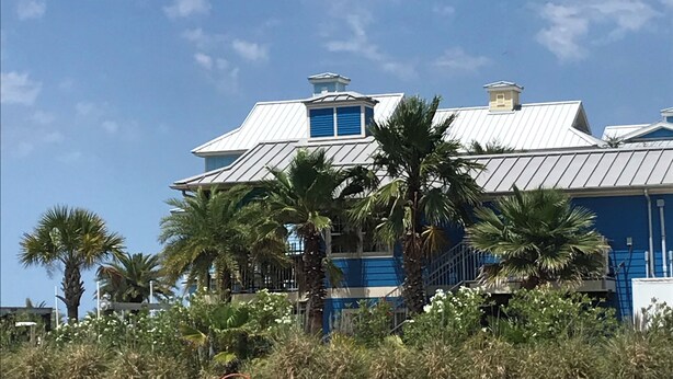 Une grande maison aux murs bleus et blancs, entourée de palmiers et sous un ciel dégagé.