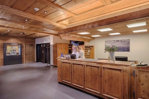 A reception area with wooden paneling, a reception desk, a wall-mounted sign, and a window with a view. - Bernerhof Swiss Quality Hotel (Saanen)