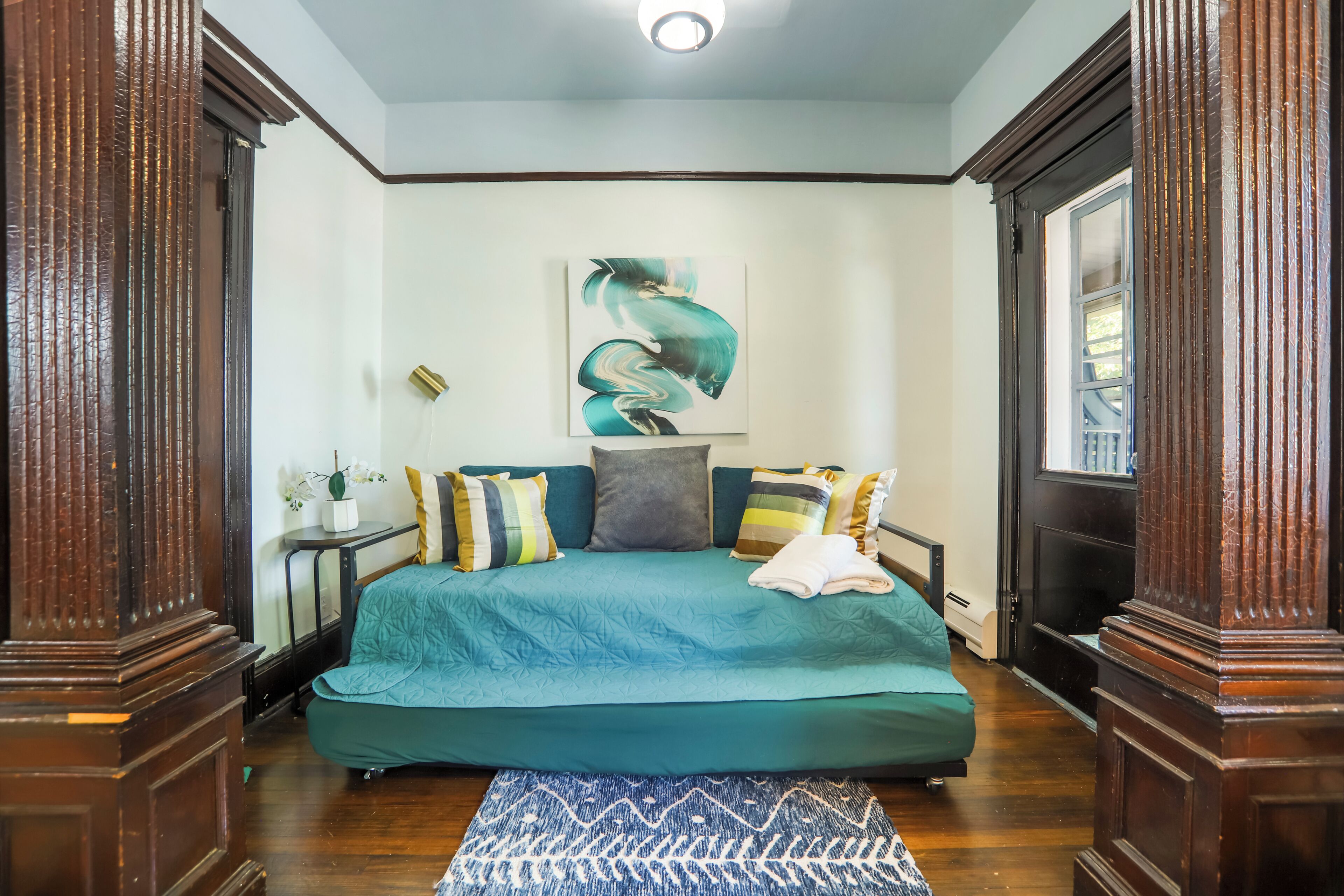 A bedroom with a teal bedspread, a decorative wall piece, and a patterned rug.