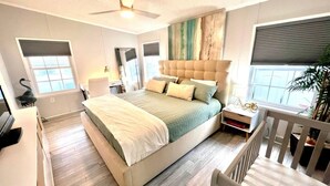 A bedroom with a large bed, a ceiling fan, and a window with blinds.
