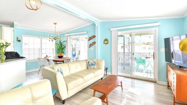 A living room with a sofa, coffee table, and a TV. There is a balcony with chairs and a table.