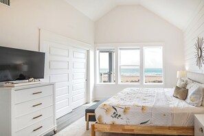 A bedroom with a bed, a TV, a dresser, and a view of the beach.