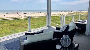 A balcony with a view of the beach, outdoor furniture, and a railing.