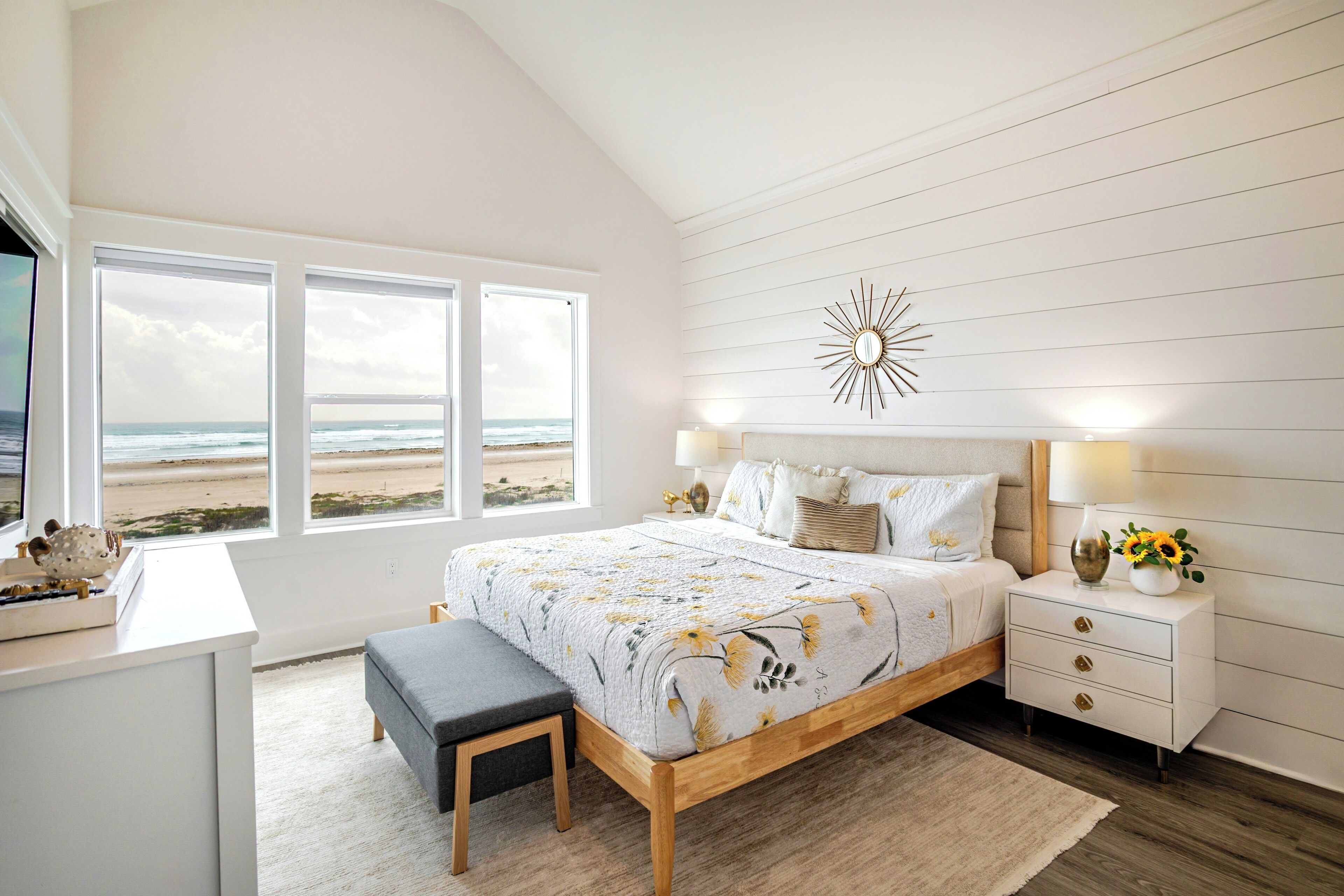 Une chambre avec un grand lit, des tables de chevet, un bureau et une vue sur la plage.