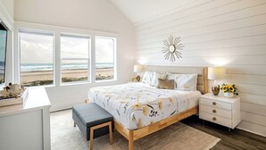 A bedroom with a large bed, bedside tables, a desk, and a view of the beach.