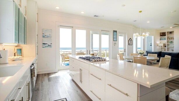 A modern kitchen with a large island, white cabinetry, and a view to the outside.