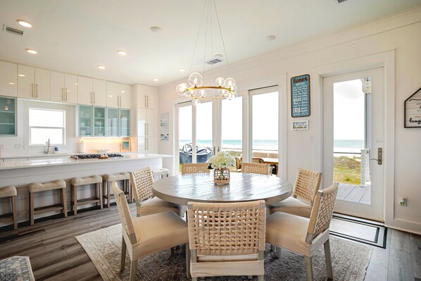A modern kitchen with white cabinets, a central island, and a dining area with wicker chairs.