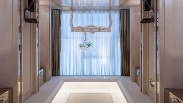 Um corredor com um caminho iluminado no centro, uma decoração suspensa e uma janela com cortinas.