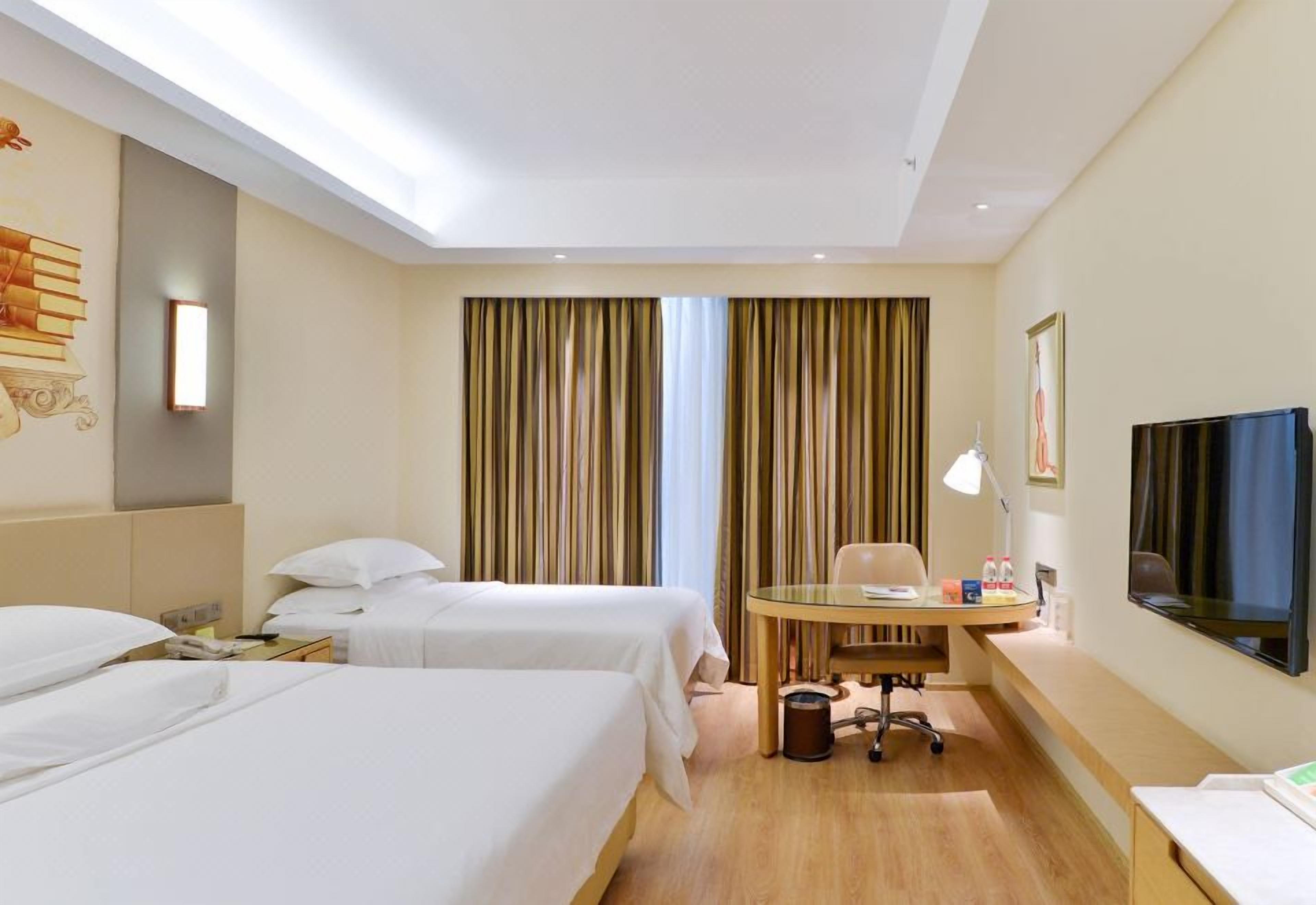 A hotel room with two beds, a desk, a chair, a TV, and a window with curtains.