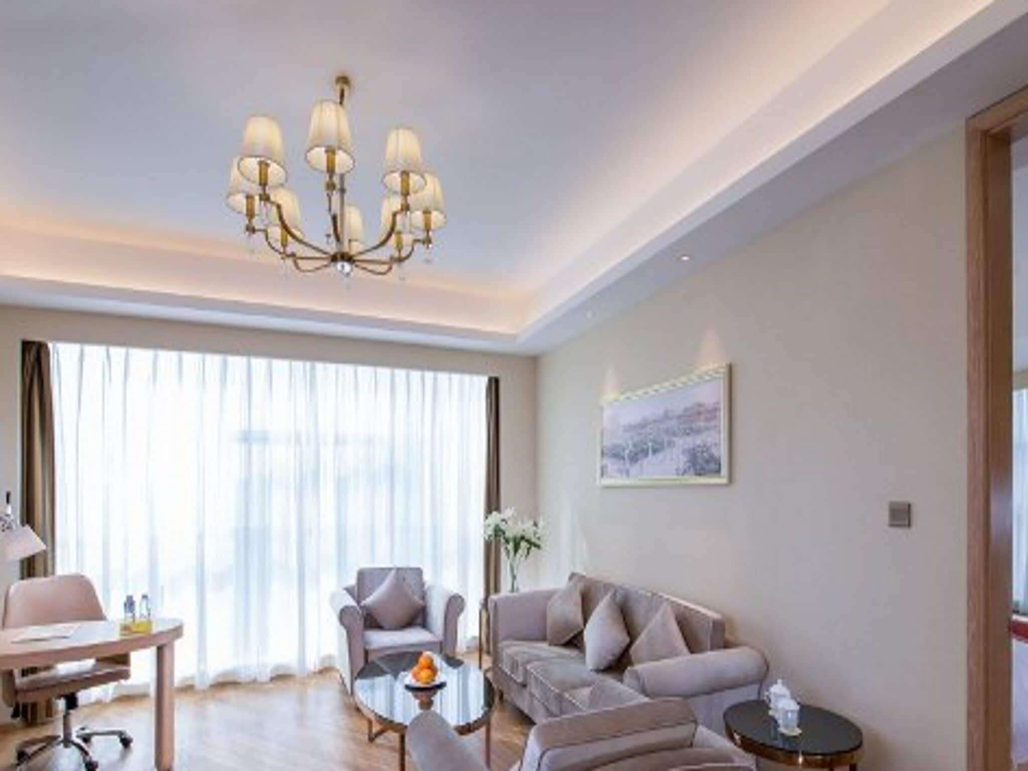 A modern hotel room with a chandelier, a sofa, a coffee table, and a desk.