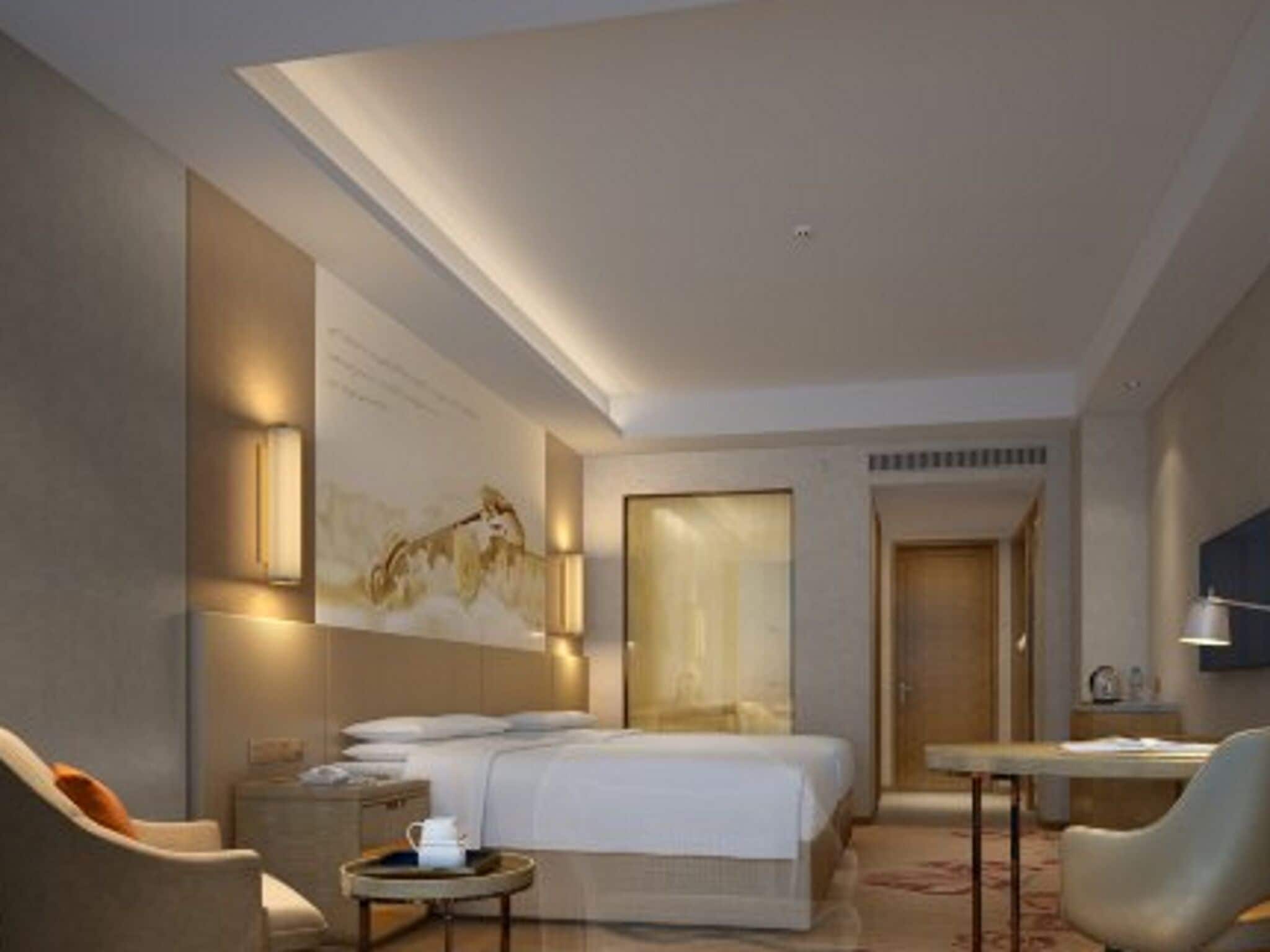 A modern hotel room with a bed, a desk, a chair, and a small table.