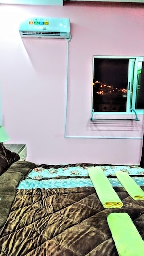Ein Zimmer mit einem Bett, einem Fenster und einer an der Wand befestigten Klimaanlage.