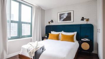 A neatly made bed with white and mustard pillows, a teal headboard, and a bedside table with a lamp and a book.