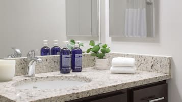 A bathroom with a granite countertop, dark cabinets, a large mirror, and a potted plant.