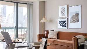 Una sala de estar moderna con un sofá, una mesa de centro, una computadora portátil y vistas a la ciudad a través de amplias ventanas.