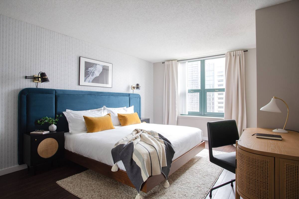 Une chambre bien rangée, avec un lit, des tables de chevet, un bureau et une fenêtre avec des rideaux.
