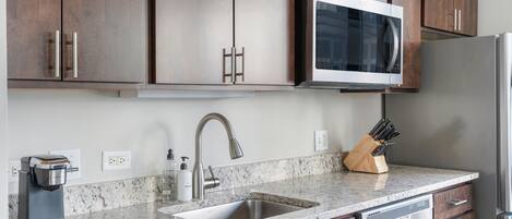 A kitchen with dark wood cabinets, a stainless steel refrigerator, a built-in microwave, a coffee maker, and a knife block.