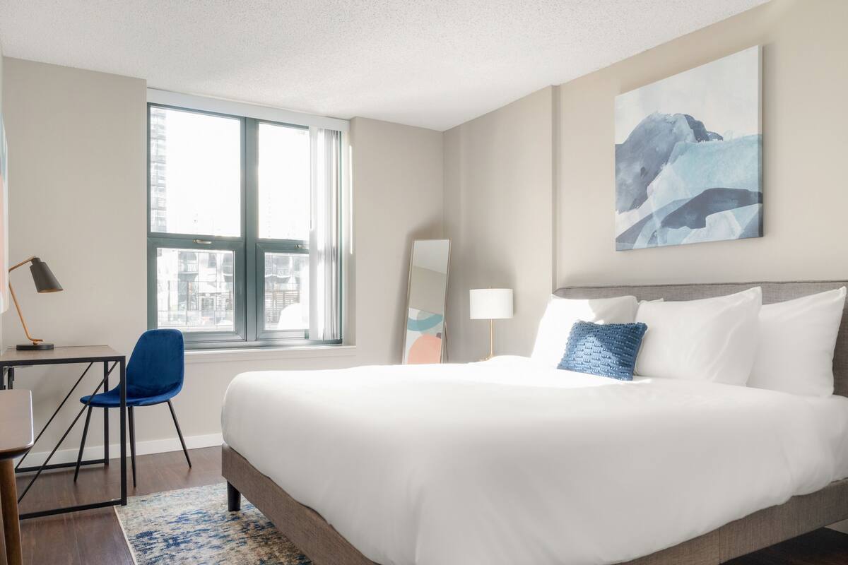 Une chambre d’hôtel avec un grand lit, un bureau avec une chaise, une fenêtre avec des rideaux et un tableau au mur.