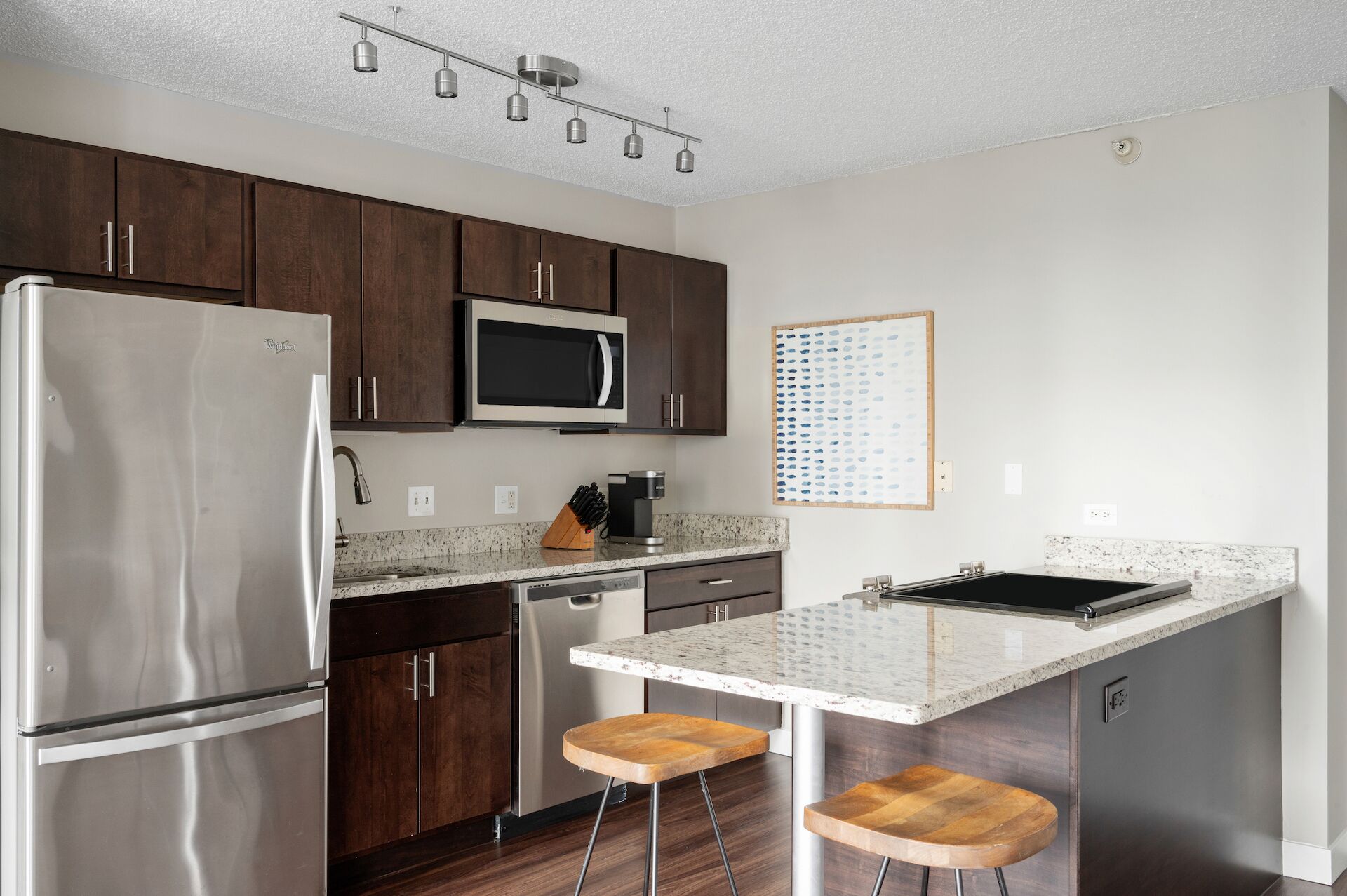 A modern kitchen with dark wooden cabinets, stainless steel appliances, a granite countertop, and a bar area with stools.