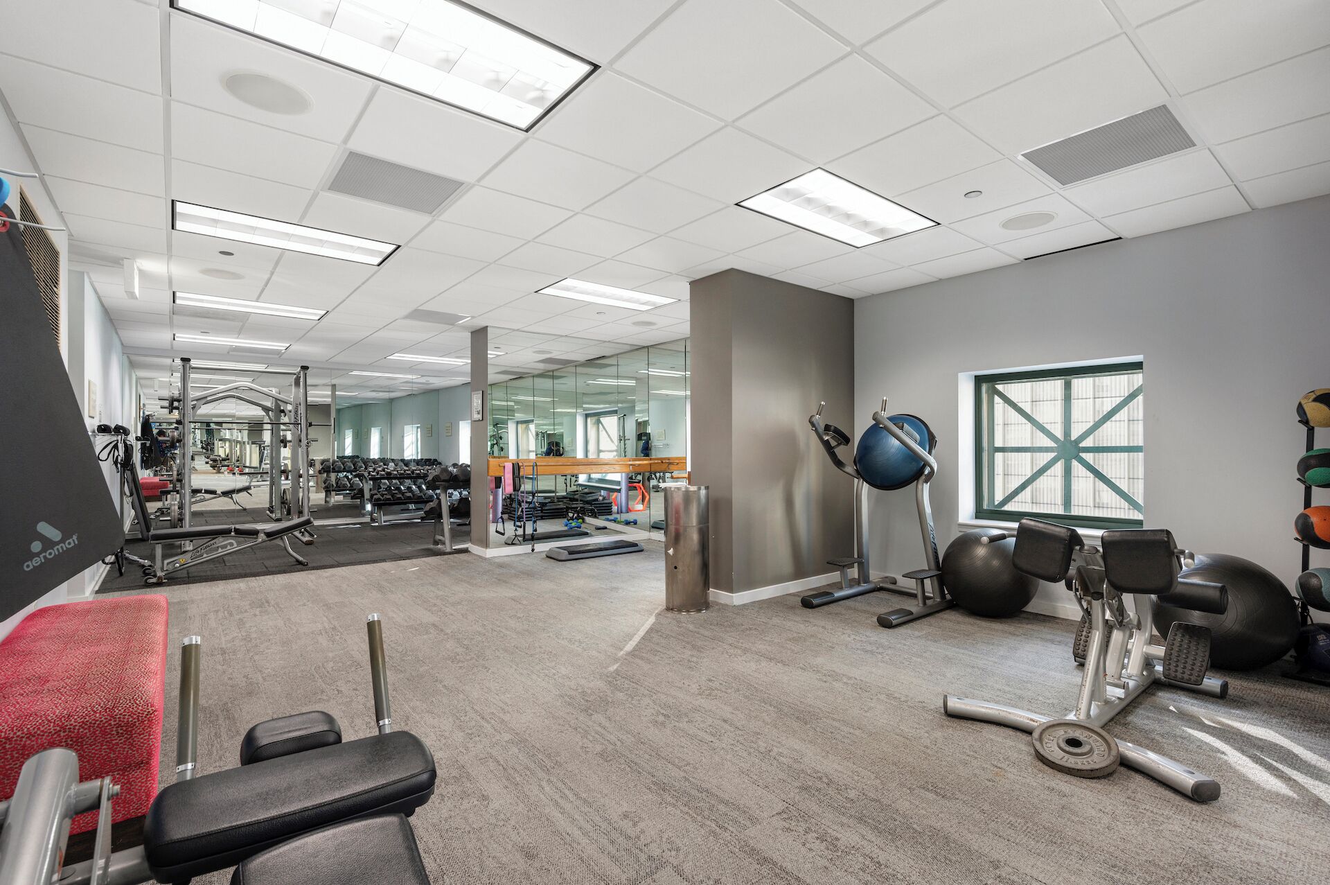 A gym with various exercise equipment, a mirror, and a window.