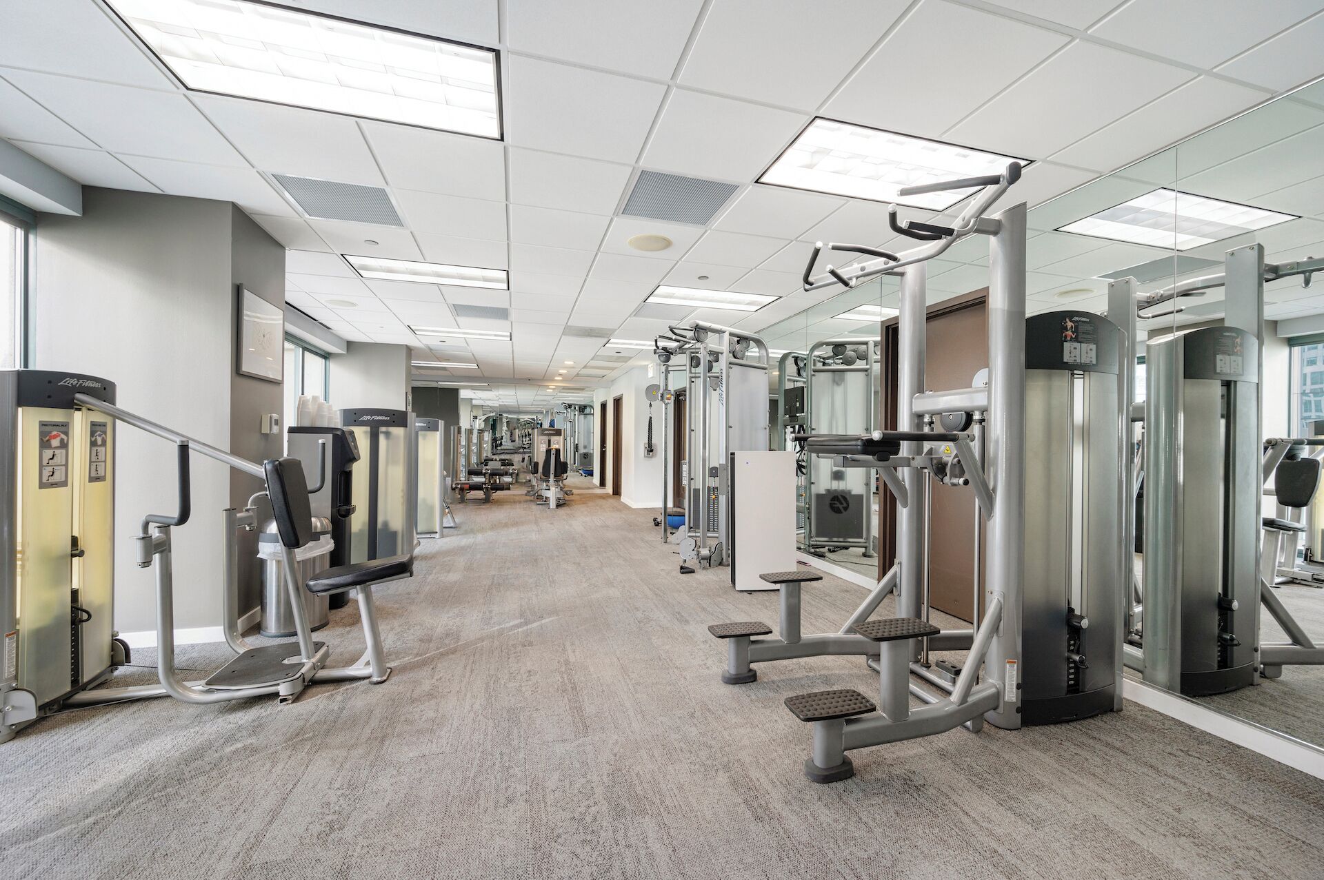 A gym with various exercise machines, a mirrored wall, and a carpeted floor.