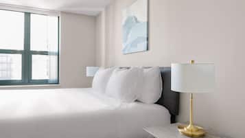 Habitación de hotel con una cama grande, una mesita de noche con lámpara, una ventana con cortinas y un cuadro colgado en la pared.