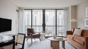A modern living room with a flat-screen TV, a brown leather chair, a round coffee table, and a sofa with a white cushion.