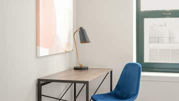 A room with a desk, a blue chair, a floor lamp, and a window with blinds.
