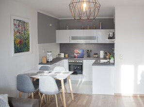 A modern kitchen with white cabinets, a dining table with chairs, and a hanging light fixture.