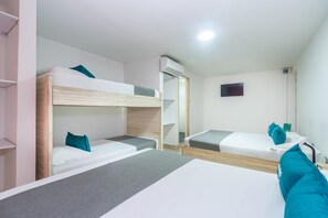 A hotel room with bunk beds, a flat bed, a TV, and an air conditioning unit.