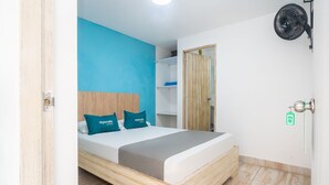 A bedroom with a bed, a blue wall, a wooden headboard, and a fan. - Ayenda Malaki (Medellín)