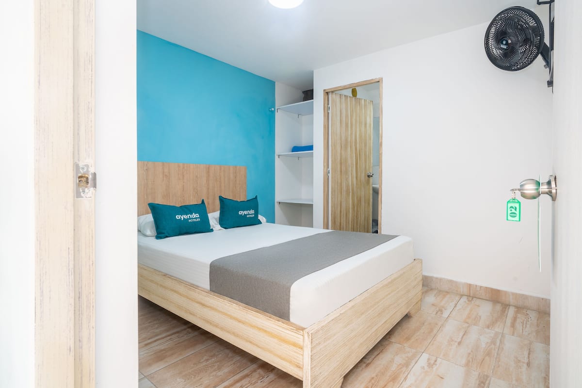 A bedroom with a bed, a blue wall, a wooden headboard, and a fan.