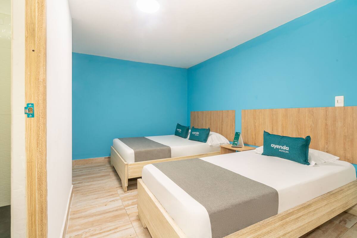 A hotel room with two beds, each with a wooden headboard, a blue wall, and a wooden floor.