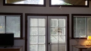 Ein Zimmer mit Fernseher auf einer Holzkommode, einer Tür mit Fenster und einer Lampe auf einem Holztisch.