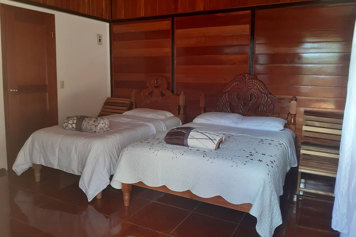 A room with two wooden beds, a wooden wardrobe, and a tiled floor.