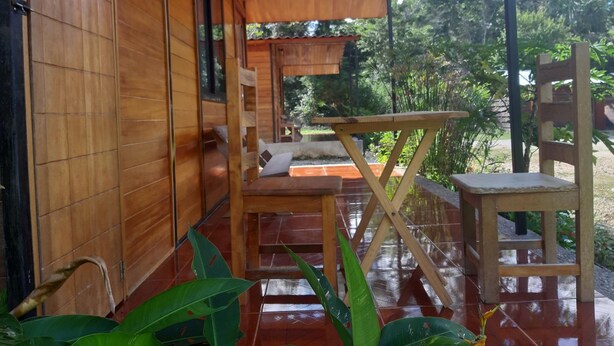 A wooden exterior with a covered patio area, including a table and chairs. - Cabaña Luna Roja (Ocosingo)