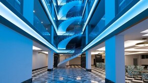 Um interior moderno com uma escadaria espiral central, piso xadrez e detalhes em iluminação azul.