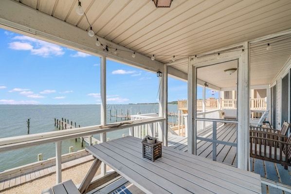 A wooden deck with a table and chairs, overlooking a body of water with docks and a pier.