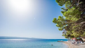 Ein Strand mit klarem Wasser, einigen Personen und einer von Bäumen gesäumten Uferlinie.