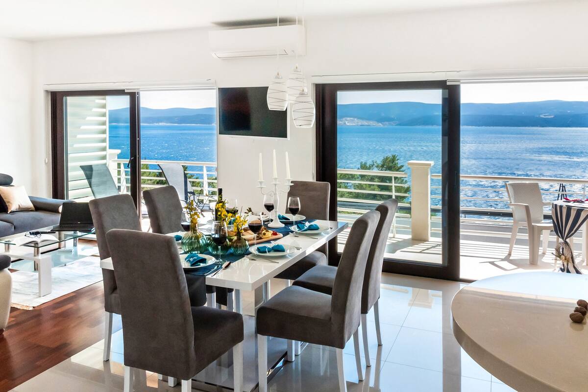 A modern living room with a dining area and a balcony overlooking a body of water.