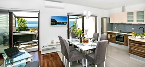 A modern kitchen with a dining area, a laptop on a glass table, and a view of the sea through the window. - Adria Croatica (Omis)